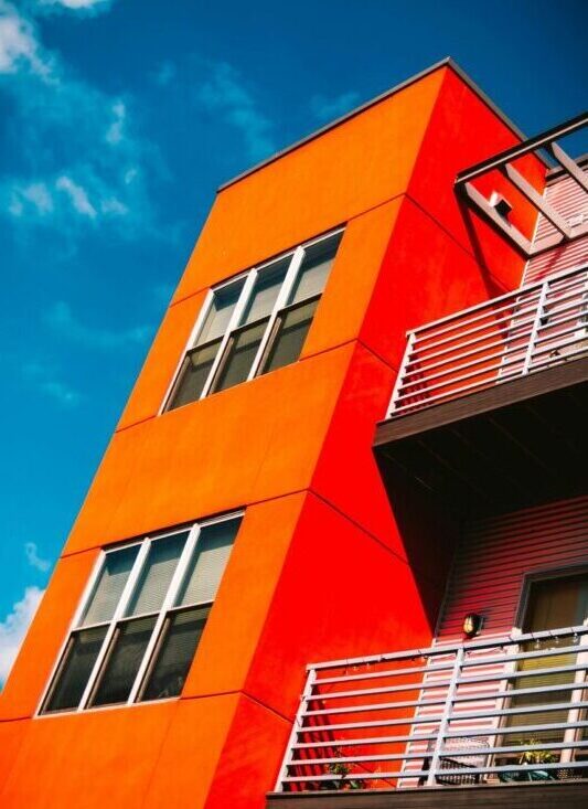 Low angle of a vibrant orange modern apartment building against a bright blue sky in Eau Claire.